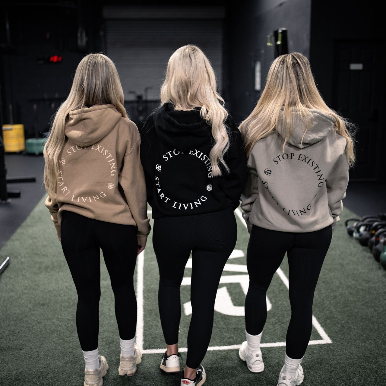 Three women wearing hoodies with text in a gym setting