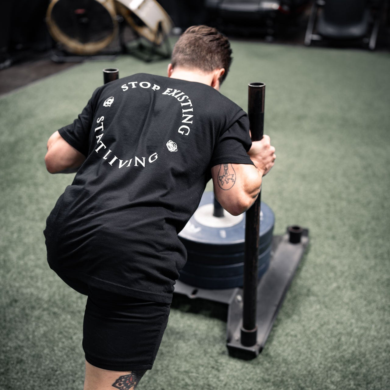 Person exercising with a weight on a green floor, wearing a black t-shirt with text.