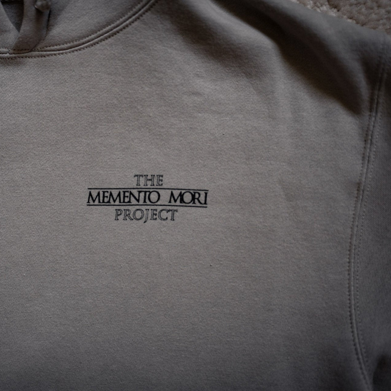 Gray hoodie with 'The Memento Mori Project' logo on a plain background